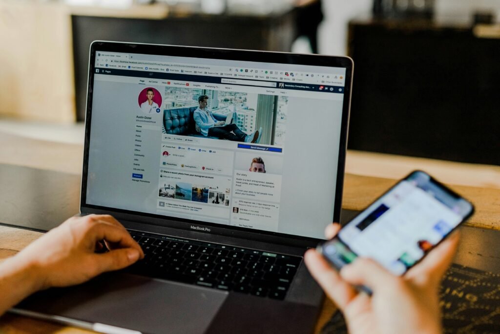 Personne utilisant un ordinateur portable avec une page de profil de réseau social ouverte tout en tenant un smartphone affichant une autre application.